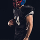 confident handsome american football player with ball looking away on black - PhotoDune Item for Sale