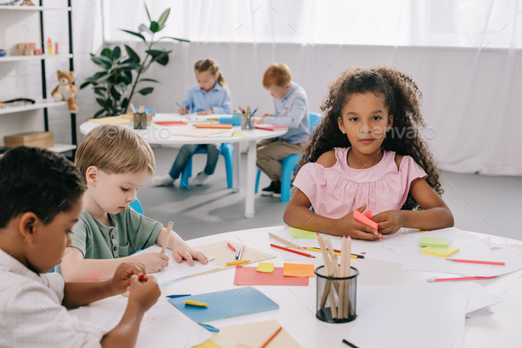 multicultural preschoolers drawing pictures with pencils in classroom ...