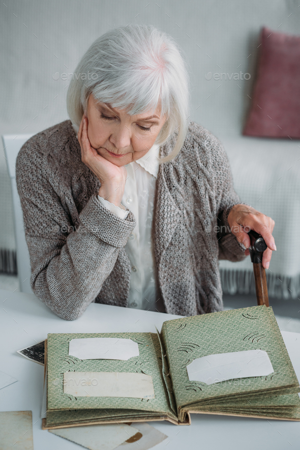 portrait of grey hair woman looking at photos in photo album at table at home