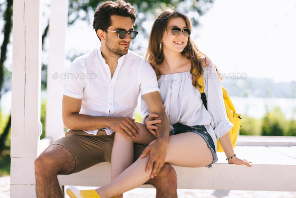 couple sitting on wooden bench at city beach and boyfriend touching ...