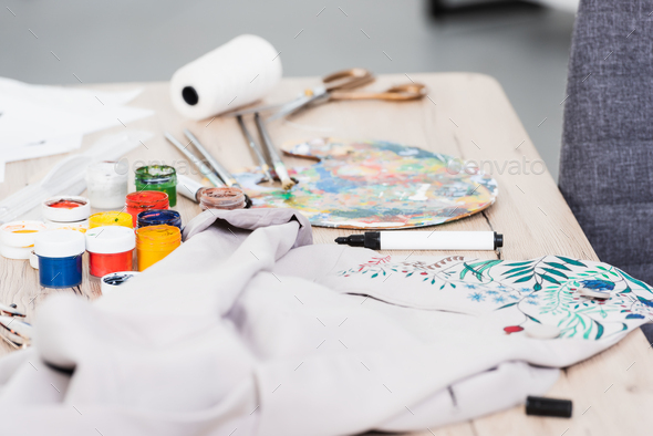 selective focus of colorful paints and painting jacket at table in clothing design studio