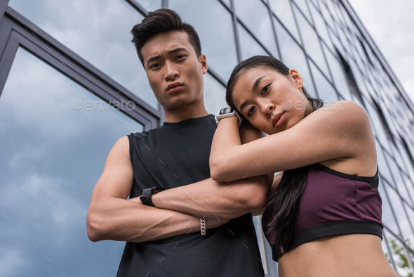low angle view of serious asian sportsman with crossed arms and sportswoman standing together and
