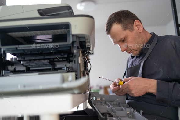 printer repair technician. A male handyman inspects a printer before starting repairs in a client's