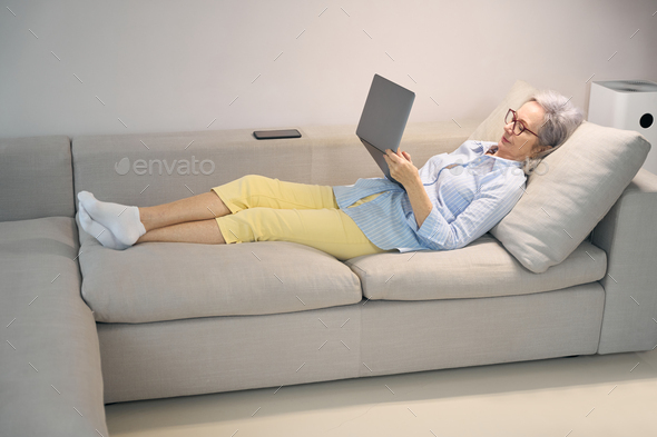 Calm pensioner lies with a laptop on couch at home