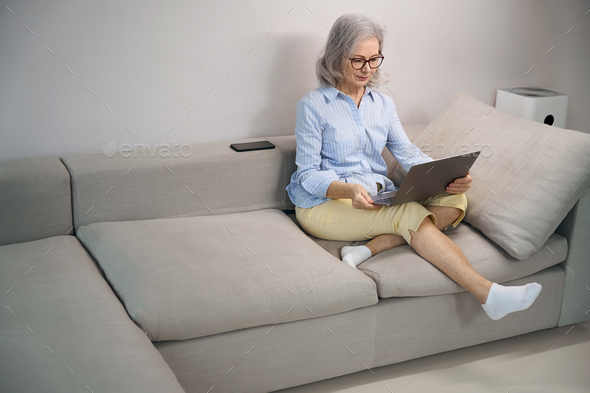 Pensioner comfortably settled down with a laptop on sofa home