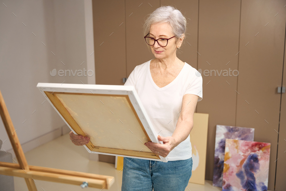 Smiling elderly lady holds canvas on stretcher in her hands