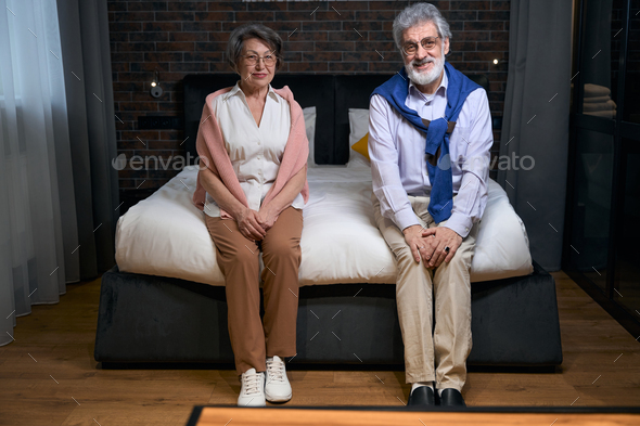 Satisfied mature married couple settled down on a large bed