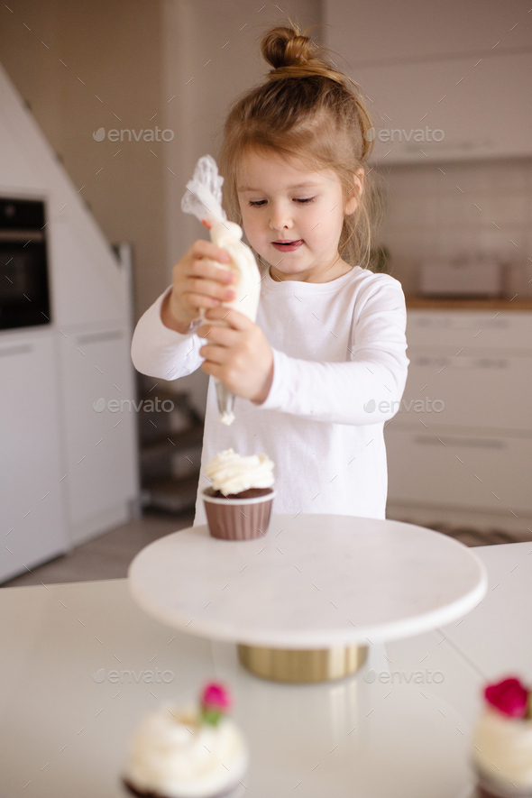 Little kid girl making cupcakes with cream cheese at home - Stock Photo - Images