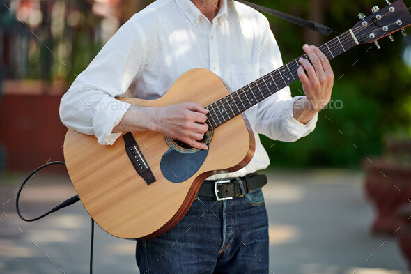 Man playing electro acoustic guitar at outdoor event, free musical performance of street musician