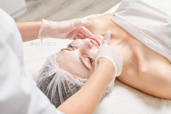 Cosmetologist massages cream mask into woman face skin for rejuvenation, procedure in beauty salon - Stock Photo - Images