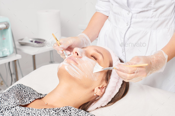 Beautician applying cosmetic cream mask on woman face for rejuvenation, procedure in beauty salon - Stock Photo - Images