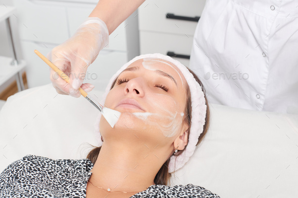Cosmetologist applying cosmetic cream mask on female face for rejuvenation procedure in beauty salon - Stock Photo - Images