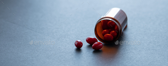 Red capsule pills and brown plastic bottle on dark background. Pharmacy banner. Prescription drugs. - Stock Photo - Images