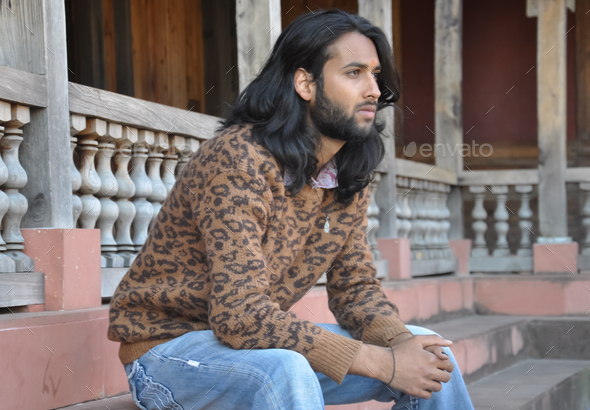 Side view of a good looking long haired Indian young guy, looking sideways while sitting in temple