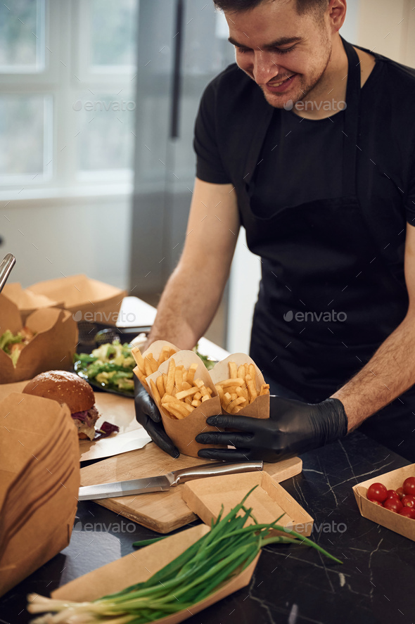 Holding French fries. Man is packing food into the paper eco boxes ...