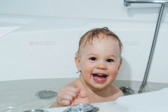 A small smiling beautiful baby bathes in a white bath. Cheerful photography. - Stock Photo - Images