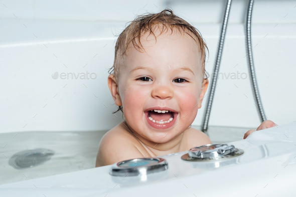 A small smiling beautiful baby bathes in a white bath. Cheerful photography - Stock Photo - Images
