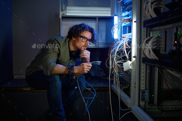 Male network engineer connecting cables in server room - Stock Photo - Images