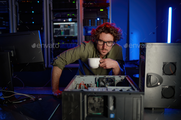 Repairman with cup of coffee looking at disassembled computer system unit - Stock Photo - Images