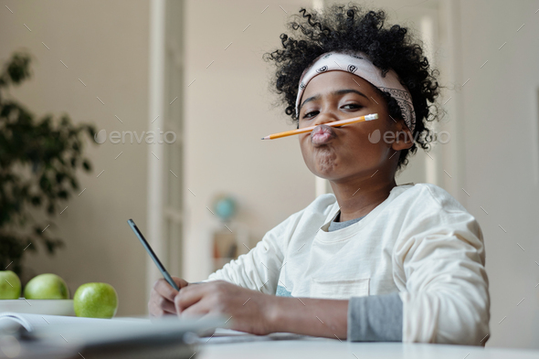 Funny schoolboy in headband holding pencil between upper lip and nose