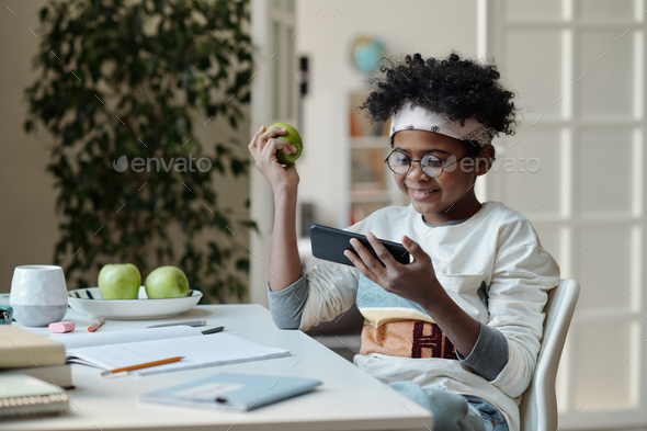 Happy schoolboy with green apple watching online video in smartphone - Stock Photo - Images