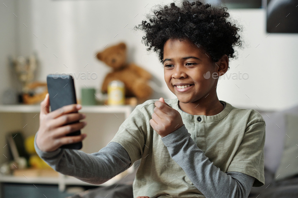 Happy schoolboy holding smartphone in front of himself and taking selfie - Stock Photo - Images