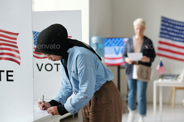 Young Muslim woman in hijab bending over vote booth and making her choice - Stock Photo - Images