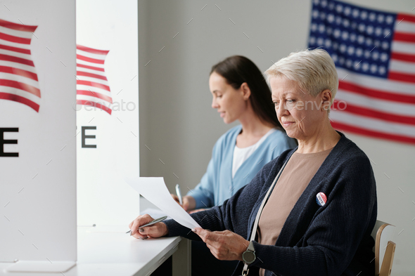 Mature female voter looking through list of candidates while sitting by ...