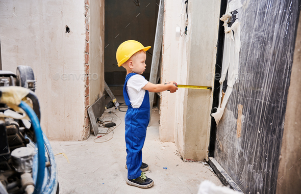 Baby boy with tape measure standing in apartment under renovation.