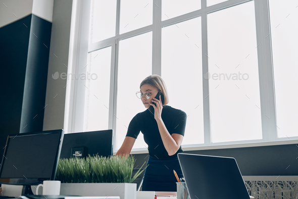 Confident young businesswoman talking on mobile phone while working in the office - Stock Photo - Images