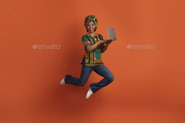 Happy traditional african woman jumping with open laptop