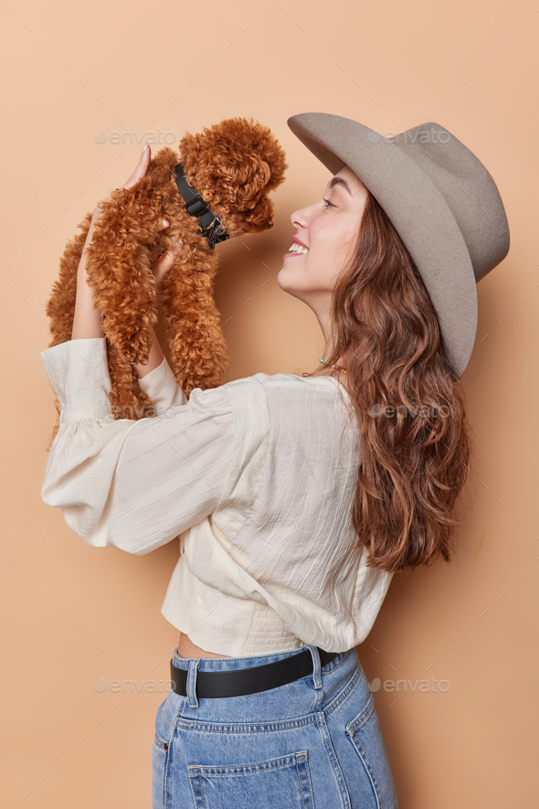 Vertical shot of cheerful woman plays with cute poodle puppy enjoys company of best friend shows