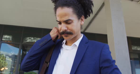 Mixed race man with moustache walking on the street and using smartphone alt