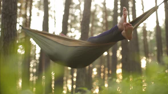 A Side View of a Bare Feet Travellet Relaxing in a Green Hammock in the Wood