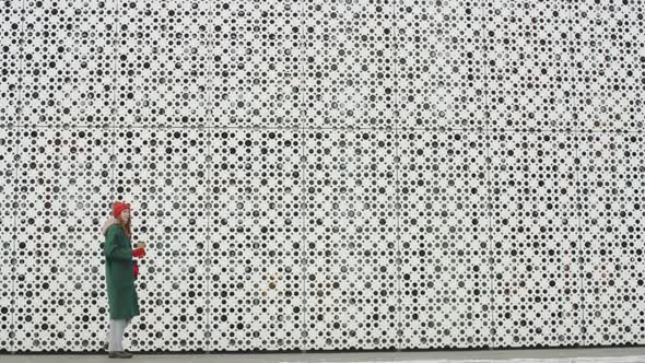 Woman Walking with Coffee along Modern Building alt
