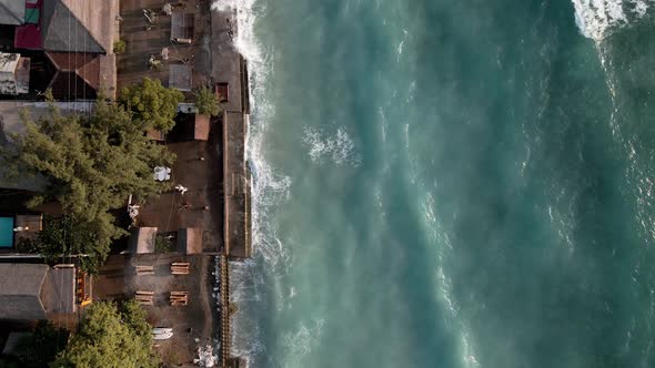 Ascending aerial top down of crashing waves at shore during sunrise on Gili Air. alt