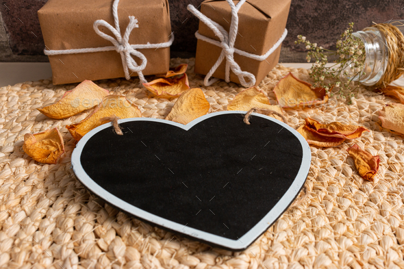 Black heart-shaped board on the round jute table mat decorated with dried rose petals