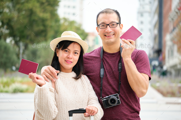 Multiracial couple of tourists smiling, holding passports and looking at camera.