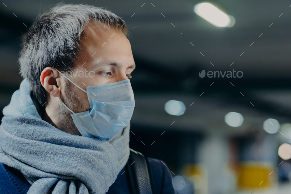 man wears protective mask against new coronavirus from China, wrapped scarf around neck