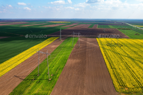 Aerial shot of transmission towers electricity pylons with power lines in cultivated field - Stock Photo - Images