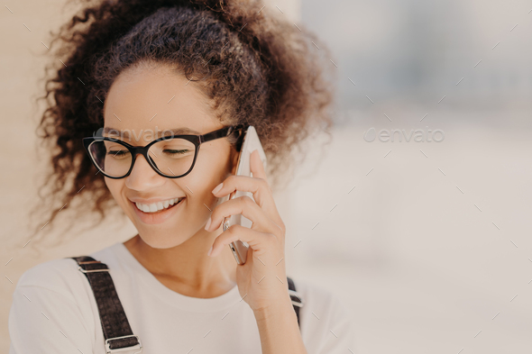 cheerful woman with crisp hair, satisfied with tariffs for telephone call, focused down - Stock Photo - Images