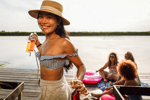 Young woman bringing drinks to her friends sitting on the pier by the lake.