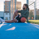 Afro Latin man with a ball sitting on a basketball court at sunset - PhotoDune Item for Sale