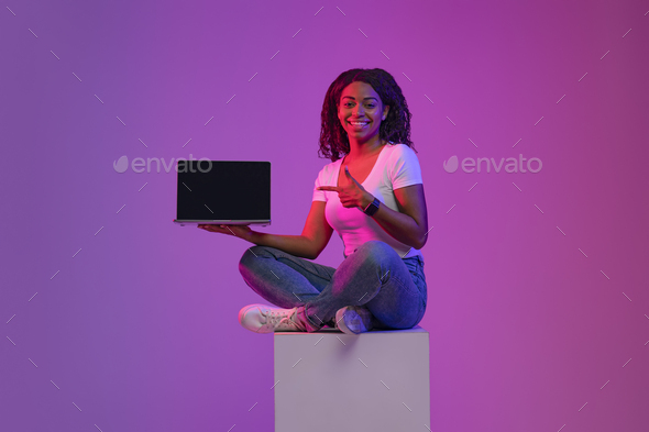 Great Website. Smiling Black Woman Pointing At Blank Laptop In Neon Light
