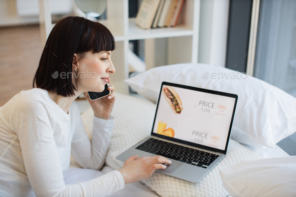 Woman talking on mobile and buying food online on laptop