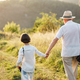 Backside photo of a little boy with his grandfather walking in a field at summer - PhotoDune Item for Sale