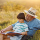 Little boy with his grandfather reading a book in a field at summer - PhotoDune Item for Sale