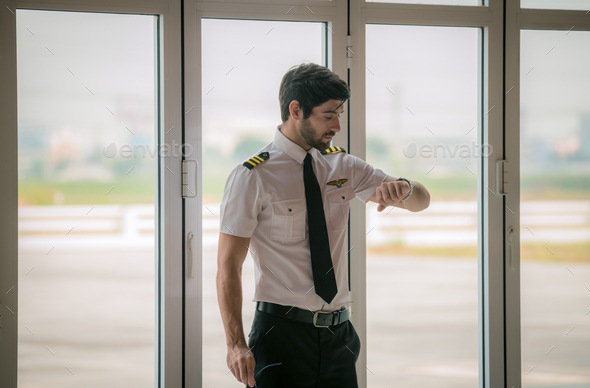 pilot in white shirt uniform and hat standing folded hand at helicopter platform background.Handsom