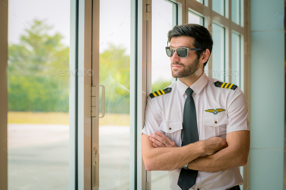  pilot in white shirt uniform and hat standing folded hand at helicopter platform background.Handsom