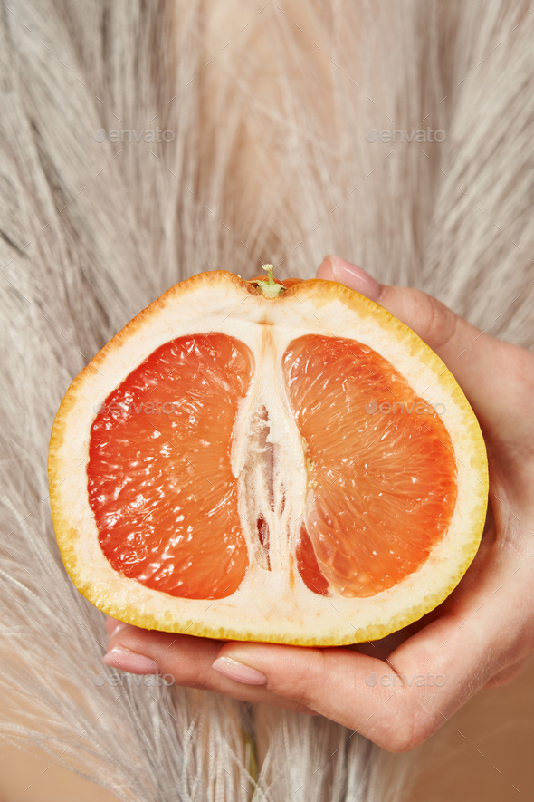 half of a cut grapefruit in a female hand, symbolizing the female genital organs